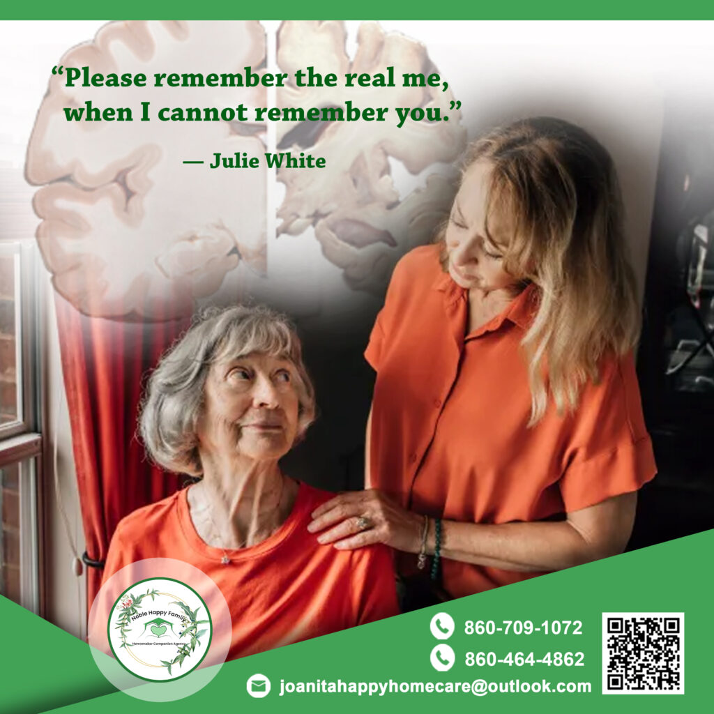 A warm, emotional moment between an elderly woman with gray hair sitting by a window and a younger female caregiver standing beside her, both wearing orange. The caregiver gently rests her hand on the older woman’s shoulder as they look at each other with affection. In the background is a faded illustration of the human brain, symbolizing memory loss or Alzheimer’s. A quote on the image reads, “Please remember the real me, when I cannot remember you.” — Julie White. The Noble Happy Family Homecare logo and contact information are displayed at the bottom.